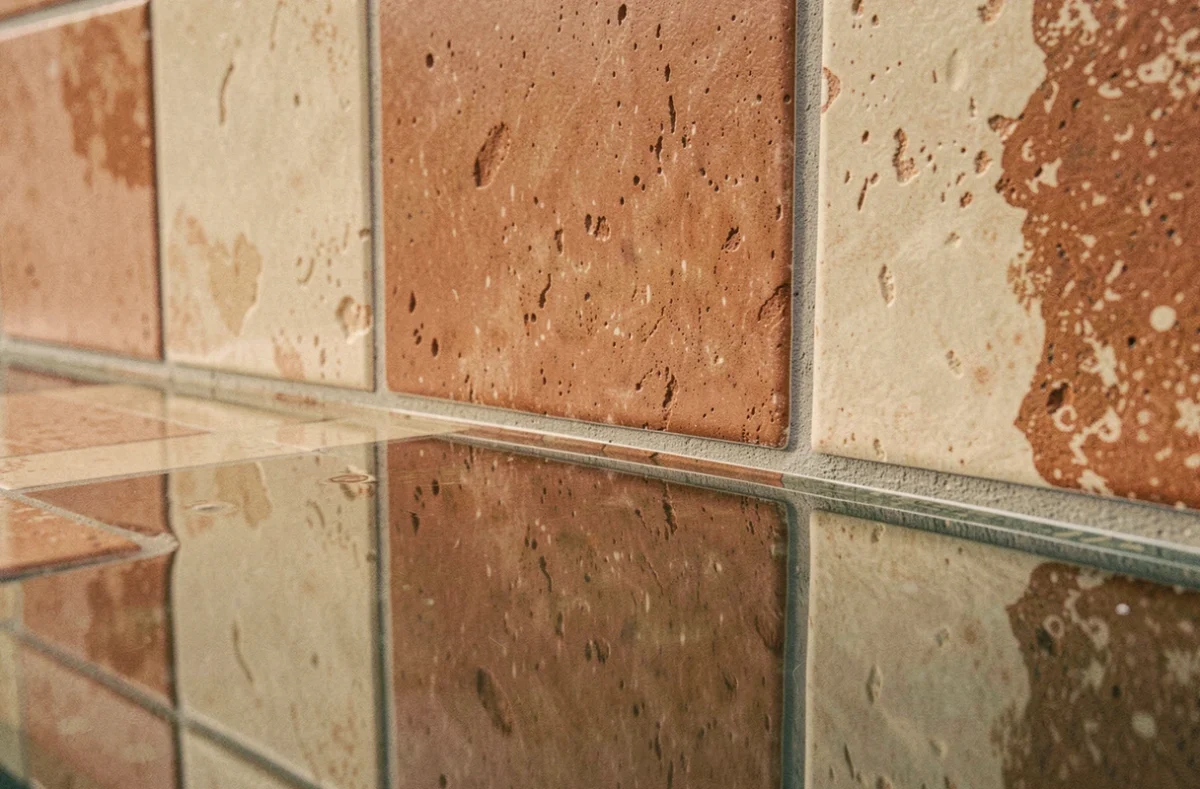 Gros plan sur des carreaux de piscine en céramique artisanale beige et terracotta avec joints gris fins