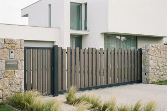 Portail en aluminium anthracite adapté à un terrain en pente devant une maison contemporaine à façade blanche